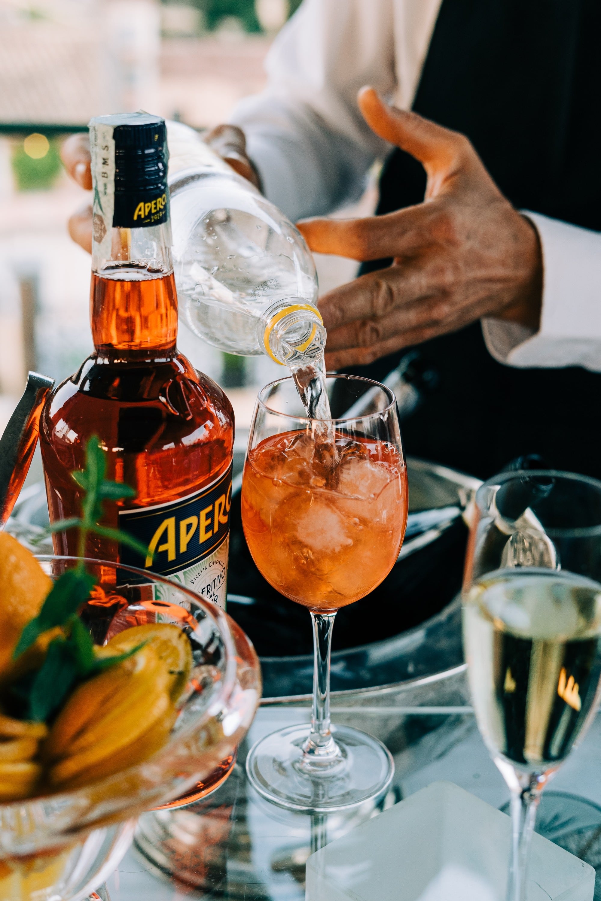 bartender pouring the soda water into the Aperol spritz