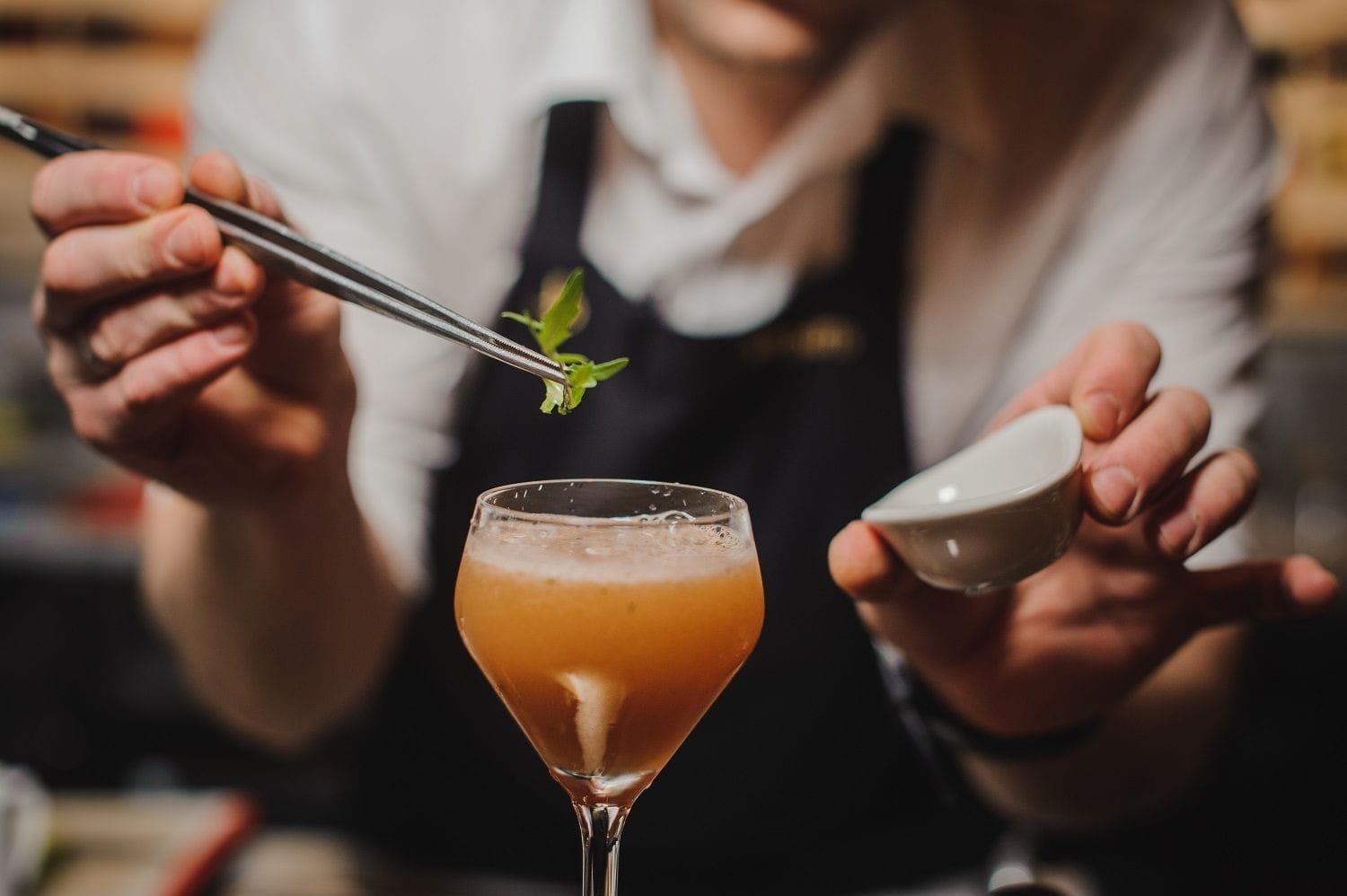 a bartender is placing a mint leaves on the cocktail by using the tweezers